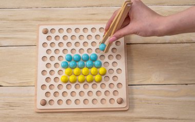Eğitim oyunu, Montessori sistemine göre sıralamak için tahta tahta. Ellerinde bir topla ahşap cımbızlar.