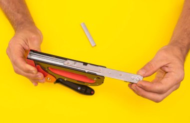 Erkek eli zımba tabancasını zımbayla doldurur. Sarı arkaplanda yakın plan..