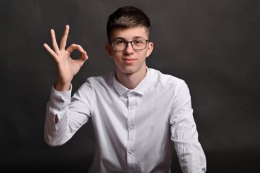 Genç adam, basit gri arkaplan üzerine kurulmuş elleriyle kendine güvenen bir 