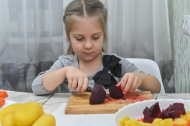 Genç bir kız mutfakta kaynamış pancar dilimleyip salata hazırlıyor. Fotoğraf, çocuklara yemek pişirme becerileri öğretme ve sağlıklı yemek hazırlama sevgisi kazandırma kavramını yansıtıyor.