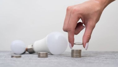 Bir LED lambası yakınında para organize eden bir kadın tasarruf ve çevre dostu teknolojiyi temsil ediyor. LED teknoloji enerji verimliliği, para ise finansal planlamayı ve sürdürülebilir yaşamı simgeler..