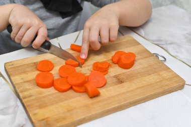 Küçük aşçılar havuç doğrarken konsantre olurlar. Çocukluk maceralarını ve beceri geliştirmeyi gösteren samimi bir an. Kültürel aşçılık geleneği ele geçirildi 