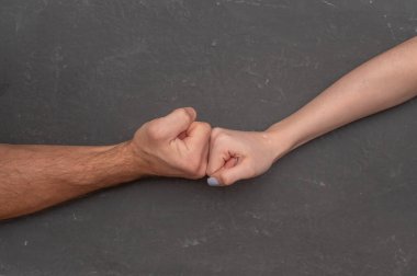 Gri arka planda kadın yumruğuna karşı erkek yumruğu, çatışmayı ve karşıtlığı simgeleyen yoğun fiziksel gerilim. Cinsiyetler arasındaki güç mücadelesi bastırılmış ellerle gösterilir