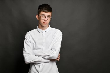 Şık gözlüklü genç adam kollarını tarafsız gri arka plana karşı sıkıca bağlamış duruyor. Çapraz kollar ve doğrudan bakışlar kapalı set ve kişisel alan farkındalığı ve sessiz analiz.