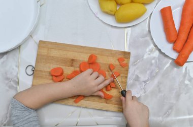 İlk güvenlik dersi: çocuk buğulanmış havuçları kesmek için kör bıçak kullanır. Çocukların yemek pişirme sınıfı promosyonları ya da güvenlik kılavuzları için ideal bir görsel. Bir çocuğun aşçılık eğitimi