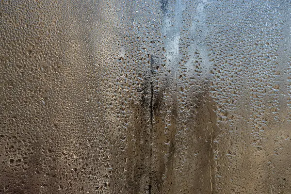 Islak cam arka plan, yoğunlaşma soğuk cam yüzeyde narin su boncukları oluşturur. Küçük damlacıklar büyüyen inciler haline gelirler yerçekimi onları aşağı çekmeden önce cam boyunca düzensiz yollarda