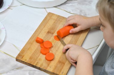 Bıçak becerilerinde ilk denemeler: çocuk yumuşak havuç sikkelerini dikkatlice keser. Yaşına uygun mutfak aktiviteleri için ebeveynlik kaynakları için ideal. konsept