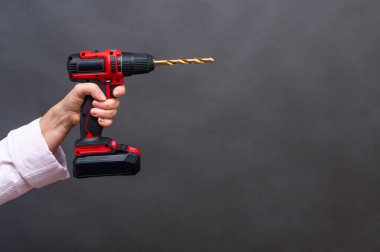 Bir kadının elindeki elektrikli tornavida, gri bir arka planda.. 