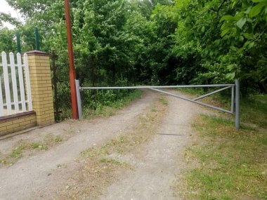 Sessiz köy bölgesinde yemyeşil ağaçlar ve yeşillik çerçeveli giriş yolu, doğa ve açık hava sadeliğiyle bağlantılı olduğunu gösteriyor. Kalın ağaçlar ve yeşilliklerle çevrili giriş. Ülke yolunda bariyer.