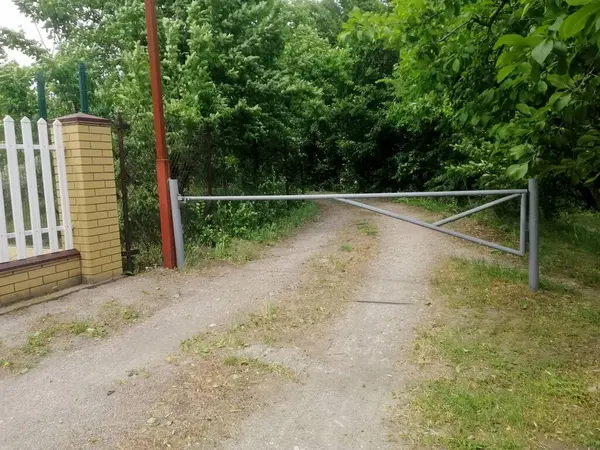 Sessiz köy bölgesinde yemyeşil ağaçlar ve yeşillik çerçeveli giriş yolu, doğa ve açık hava sadeliğiyle bağlantılı olduğunu gösteriyor. Kalın ağaçlar ve yeşilliklerle çevrili giriş. Ülke yolunda bariyer.