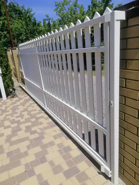 Dikey fotoğraf güzel beyaz kapı özel evde. Açık gökyüzü ve bereketli yeşillik ile parlak giriş alanı yaz sükuneti ve özel mülk erişimini çağrıştırıyor. Çitlerle çevrili güneşli özel garaj yolu