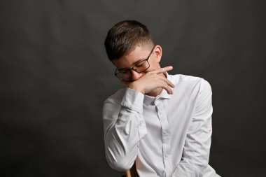 Gözlüklü, beyaz gömlekli, eli ağıza yakın poz veren genç bir adamın stüdyo portresi. Adam elleriyle ağzını kapatarak gülüyor. Vücut dili bir kavramdır. yalan söylemek ya da yalan söylemek