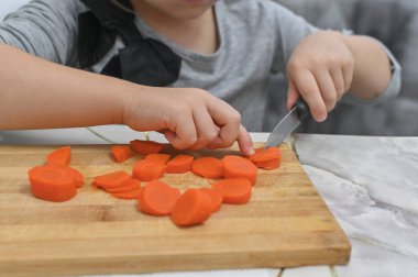 Turuncu havuç dilimleriyle kaplı ahşap kesme tahtası çocukların aşçılık gelişimini gösteriyor. Detaylı çekim ev yemeği ortamında öğrenme başarılarını vurguluyor. konsept