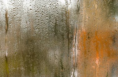 Küçük su damlacıklarıyla kaplı ıslak cam pencereler, yoğunlaşma yoluyla bulanık bir görüntü yaratıyor. İçerideki nem, şeffaf yüzeyde doğal desen oluşturur. Islak cam dokusu gösteriliyor 