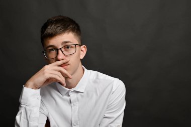 Entellektüel erkeğin düşünürken parmaklarıyla dudaklara dokunması. Gri arka plan ciddi yüz ifadelerini ve jestlerini vurgular. Gözlüklü modern adam düşüncelere dalmış, ağzı kapalı..