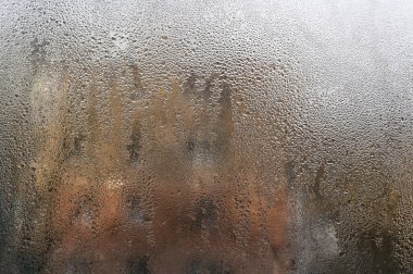 Yoğunlaşma cama sıvı desenler çizdikçe atmosferik soyutlama şekilleri oluşur. Pencere, doğanın su sanatının gösterisine dönüşür. Islak cam arka plan. buğulanmış pencere