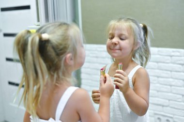 Küçük bir kız aynanın yanında dudaklarını rujla boyuyor.