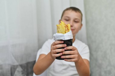Bir çocuğun ellerinde nefis bir shawarma. O aç ve ona büyük bir iştahla bakıyor..