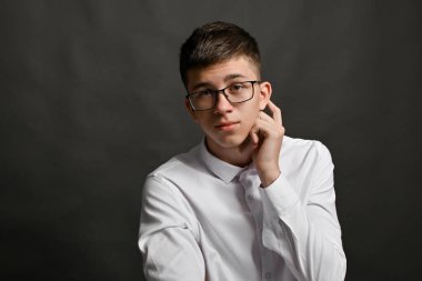 Gözlüklü ve beyaz gömlekli genç adam düşünceli bir şekilde poz veriyor, başını hafifçe çeviriyor, el kulağına dokunuyor, iç gözlem duygusunu ifade ediyor. Düşünceli, düşünceli, düşünceli.. 