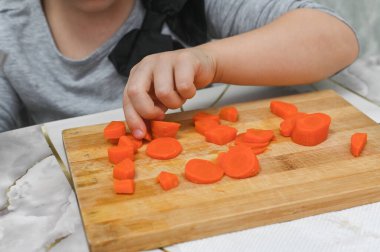 Çocuğun küçük elleri, yetişkinlerin gözetiminde yumuşak havuçlarla bıçak tekniğinde ustalaşır. Çocuklara mutfak güvenliğini öğretmek için harika bir imaj. konsept