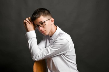 Erkek, gergin yüzüyle katlanmış kollarına yaslanır. Klasik derin düşünce ya da fantezi pozu. Aşırı düşünceli olduğunu gösteriyor. Aşırı zihinsel yüklenme göstergesi. Gri arka planda gözlüklü adam