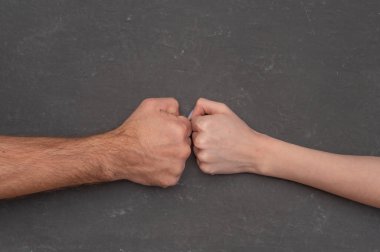 Gri arka planda kadın yumruğuna karşı erkek yumruğu, çatışmayı sembolize eden yoğun fiziksel gerilim. Kompozisyon karşıtlığa odaklanıyor. cinsiyet mücadelesi, çatışma ve çatışma kavramı.