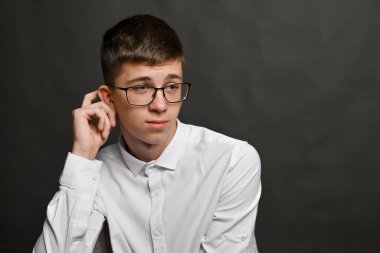Düşünceli bir poz, genç adam elini kulağının arkasında tırmaladı. Gözlüklü ergen çocuk, ifadesine odaklanmış. Vücut dili, belirsizlik jesti ve düşüncelilik. çözüm bulma kavramı