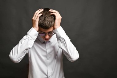 Adam kafasını iki eliyle sıkıca tutuyor, yoğun bir hayal kırıklığı, umutsuzluk ya da panik. Aşırı stres ya da psikolojik aşırı yüklenme içeren evrensel bir jest. Duygusal çöküntü ya da kafa karışıklığı yaşayan genç bir erkek. 