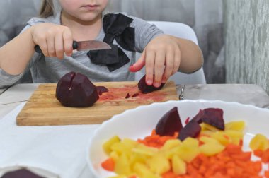 Küçük kız salata için pancar kesiyor. 