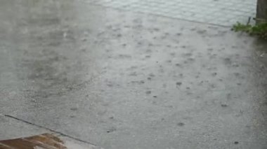 Yağmur gri asfalt kaldırıma vurur su yere düşer ve dalgalanmalar oluşturur. Doğal yağmurlu hava. Asfalt yüzeyi yağmur sırasında su birikintileri ve su damlalarıyla kaplıdır. Yağmur ve yağış kavramı