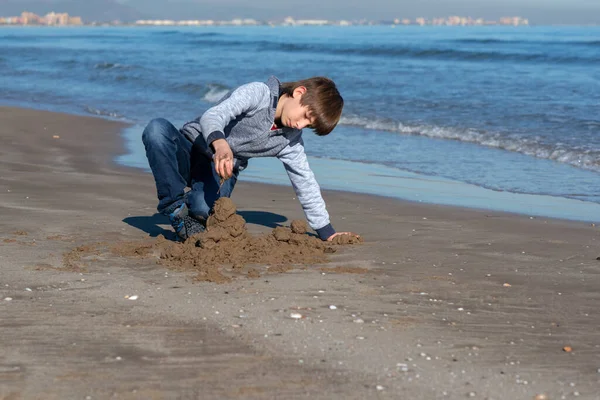 冬のビーチで遊んでいる若いハンサムな男の子 秋の海辺に砂の城を建てるかわいい幸せな11歳の少年 子供の屋外肖像画 — ストック写真