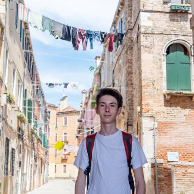 Çamaşırların üzerinde poz veren yakışıklı genç çocuk eski Venedik sokaklarında çamaşır iplerine asılıyor.