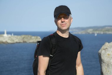Beyzbol şapkası ve sırt çantasıyla sahilde poz veren orta yaşlı bir adam, açık hava resmi. Yakışıklı, olgun bir adam. Açık hava erkek portresi. 