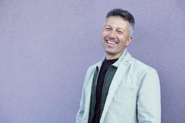 Orta yaşlı bir adam leylak rengi üzerinde poz veriyor. Yakışıklı, olgun bir adam. Açık hava erkek portresi. 