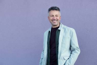 Orta yaşlı bir adam leylak rengi üzerinde poz veriyor. Yakışıklı, olgun bir adam. Açık hava erkek portresi. 