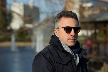 Yakışıklı, olgun bir adam. Açık hava erkek portresi. Güneş gözlüklü çekici, kendinden emin, orta yaşlı bir adam..