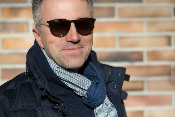 stock image Handsome man. Outdoor winter male portrait. Attractive confident middle-aged man in sunglasses posing over bricks wall, image toned.