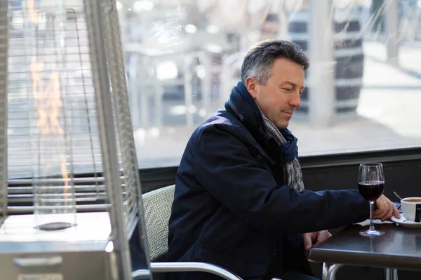 stock image Handsome man in street winter cafe drinking coffe and wine. Male portrait. Attractive confident middle-aged man sitting in city bar, image toned, image toned and noise added.