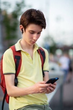 Yazın açık havada akıllı telefon kullanan genç bir çocuk. 15 yaşında bir genç konuşuyor ve cep telefonuyla mesajlar gönderiyor.