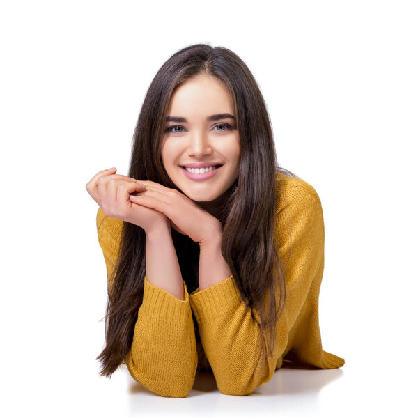 Очаровательная улыбающаяся молодая белая женщина с длинными каштановыми волосами, держащая руки аккуратно на лице, позируя на белом фоне.