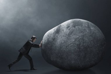 İş adamı karanlık arka planda büyük taşları itiyor