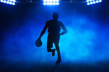 Profesyonel basketbolcunun gölgesi, koyu mavi duman arka planına damlıyor.