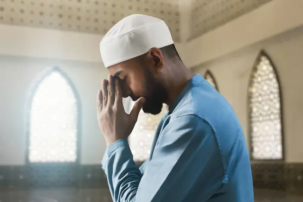 Portrait of sad crying young asian muslim man with beard praying in the mosque window arch