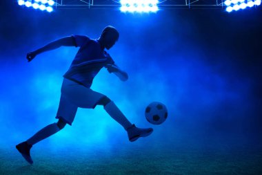 Geceleri boş stadyumda topa vuran genç profesyonel futbolcunun üç boyutlu gölgesi.