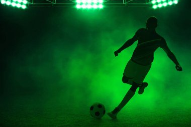Geceleri boş stadyumda topa vuran genç profesyonel futbolcunun üç boyutlu gölgesi.