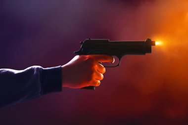 Siyah dumanlı arka planda silahlı kapüşonlu bir adam.
