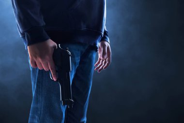 Siyah arka planda silahlı kapüşonlu bir adam.