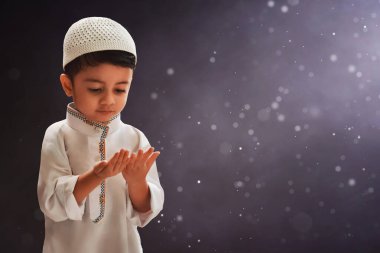 Asyalı Müslüman çocuğun portresi koyu arka planda dua ediyor, Kurban Bayramı Mübarek konsepti