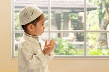 Evde pencere kenarında dua eden Asyalı Müslüman çocuğun portresi, Kurban Bayramı Mübarek konsepti