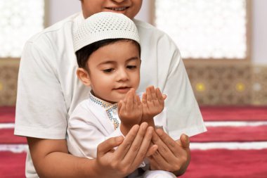 Endonezyalı Müslüman baba ve masum oğul camide birlikte oturup dua ederken gülümsüyor, Kurban Bayramı Mübarek kavramı.